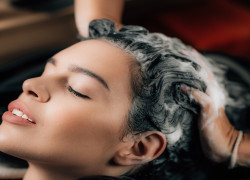 Hairdresser applying shampoo on woman’s hair in beauty salon.
